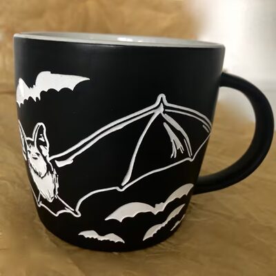 Black ceramic mug printed with a white flying bat trailed by smaller bats