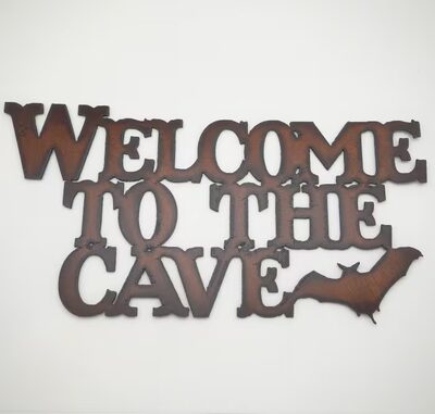 Rusted steel cut-out sign reading Welcome to the Cave with a bat silhouette